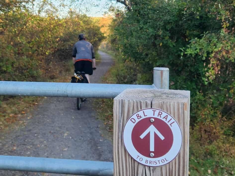 A cyclist riding down a trail with a D&L Trail Marker pointing forward towards Bristol.