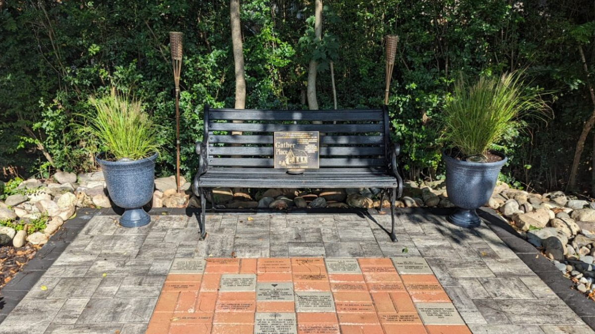 A bench between two torches and two potted plants, with engraved bricks in front.
