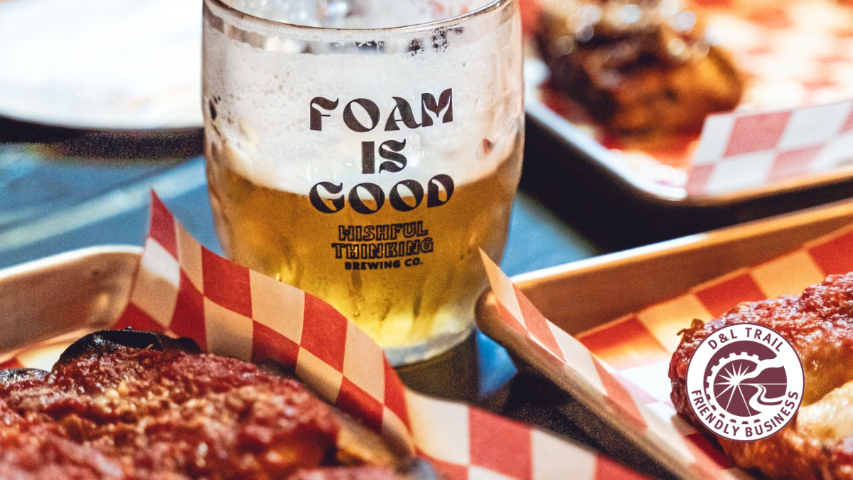 A beer mug with Foam is Good written on it, next to some pizza.