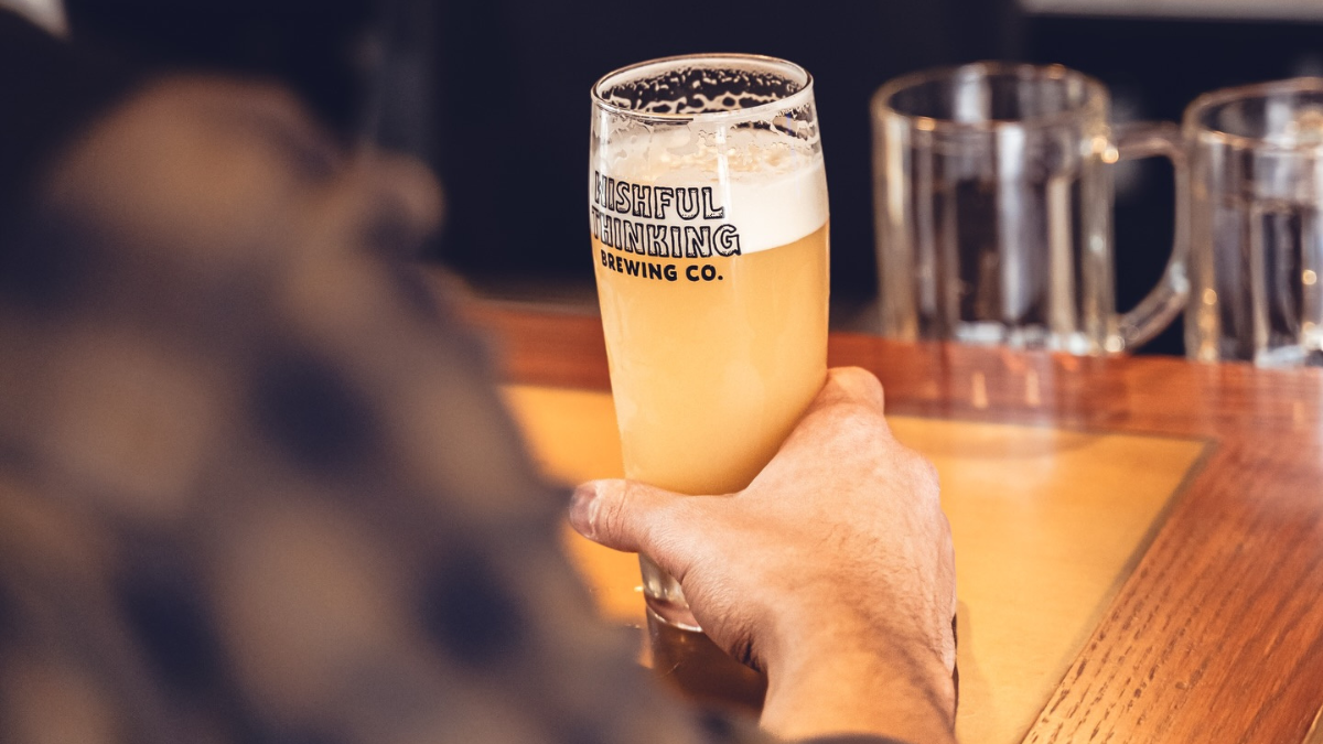 A full beer at the bar with a Wishful Thinking Brewing Company logo.